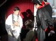 Alunos em cena de teatro com capa vermelha sob a luz do palco