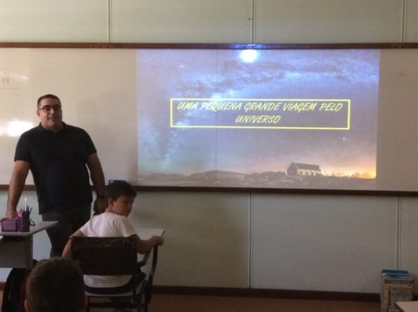 Professor diante da tela de projeção na apresentação sobre o Universo
