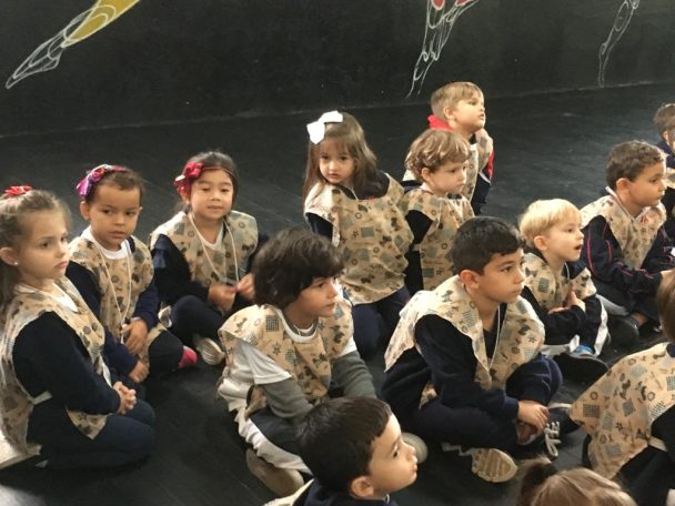 Crianças da educação infantil sentadas no chão assistindo à apresentação na Chácara Encantada