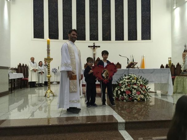 Padre e alunos diante do altar florido durante a Novena de Santa Rita