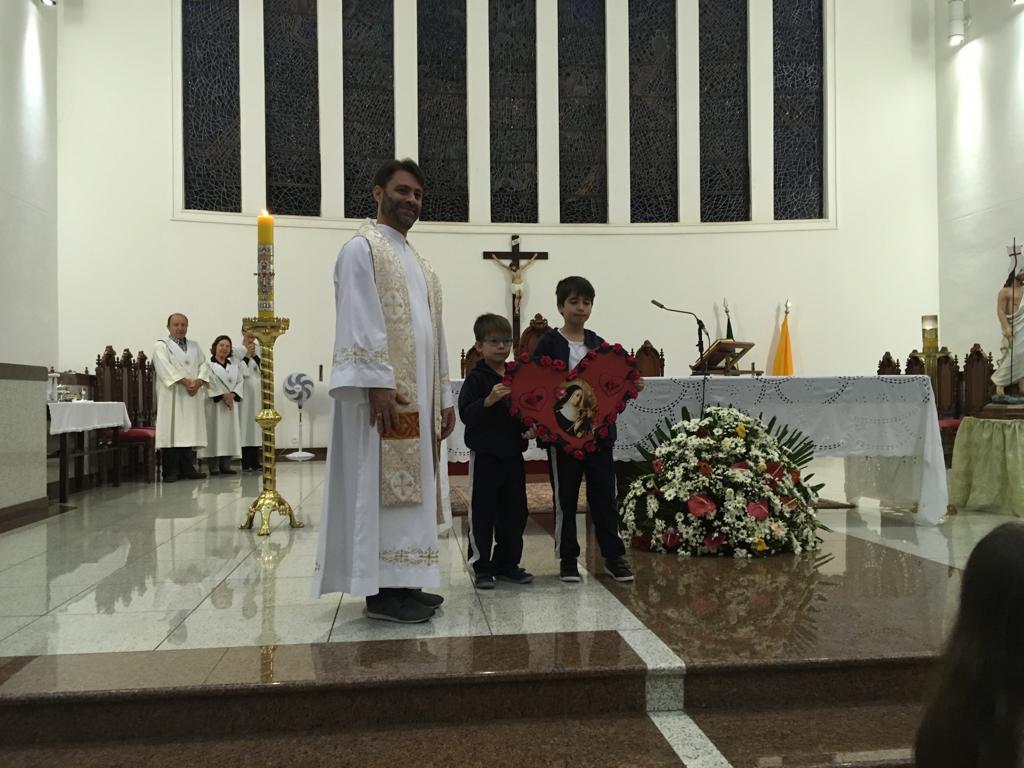Padre e alunos diante do altar florido durante a Novena de Santa Rita