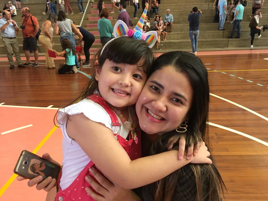 Mãe e filha abraçadas e sorrindo no evento Momentos da Mamãe, no ginásio