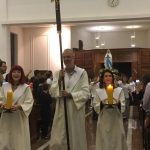 Alunos vestidos de branco em procissão pelo corredor da igreja, na Coroação de Nossa Senhora