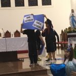 Alunos erguem cartazes azuis durante a Coroação de Nossa Senhora