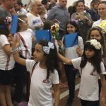 Alunos vestidos de branco em procissão pelo corredor da igreja, na Coroação de Nossa Senhora