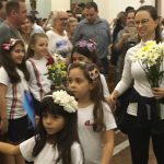 Alunos vestidos de branco em procissão pelo corredor da igreja, na Coroação de Nossa Senhora