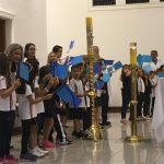 Alunos vestidos de branco em procissão pelo corredor da igreja, na Coroação de Nossa Senhora