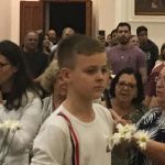 Alunos vestidos de branco em procissão pelo corredor da igreja, na Coroação de Nossa Senhora