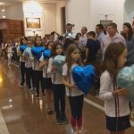 Alunos vestidos de branco em procissão pelo corredor da igreja, na Coroação de Nossa Senhora