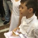 Alunos vestidos de branco em procissão pelo corredor da igreja, na Coroação de Nossa Senhora