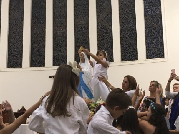 Alunos de branco com os braços erguidos durante a Coroação de Nossa Senhora