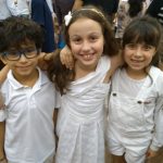 Alunos vestidos de branco em procissão pelo corredor da igreja, na Coroação de Nossa Senhora