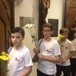 Alunos vestidos de branco em procissão pelo corredor da igreja, na Coroação de Nossa Senhora
