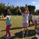 Crianças brincam com bolhas de sabão no gramado, na colônia Super Férias