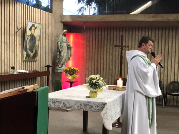 Padre falando ao microfone diante do altar na missa com o 5º ano