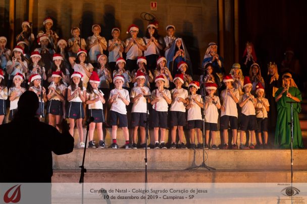 Coral de alunos com gorros de Natal no palco durante a Cantata de Natal