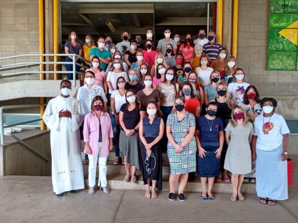 Professores e funcionários de máscara reunidos na escadaria da escola na volta às atividades