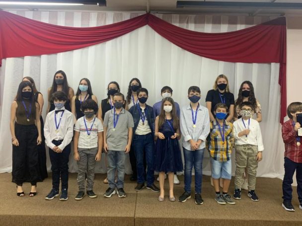 Alunos de máscara enfileirados com medalhas no palco da Noite de Premiação