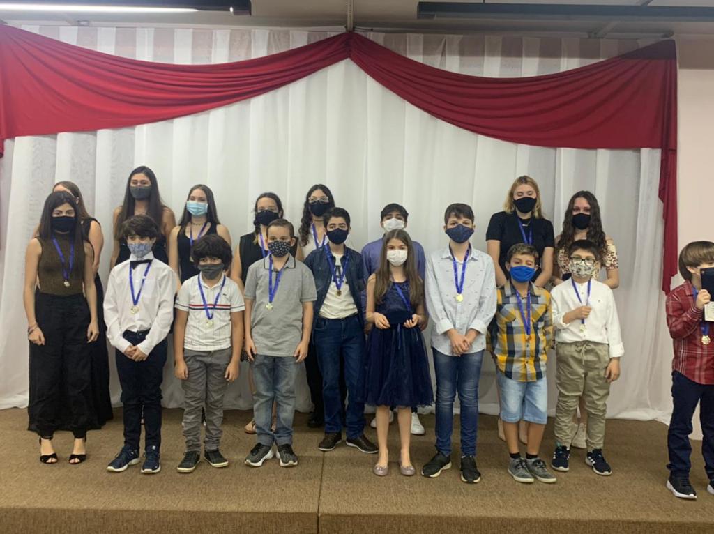 Alunos de máscara enfileirados com medalhas no palco da Noite de Premiação