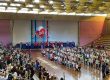 Ginásio cheio de alunos na homenagem do Dia das Mães, com um coração projetado no telão