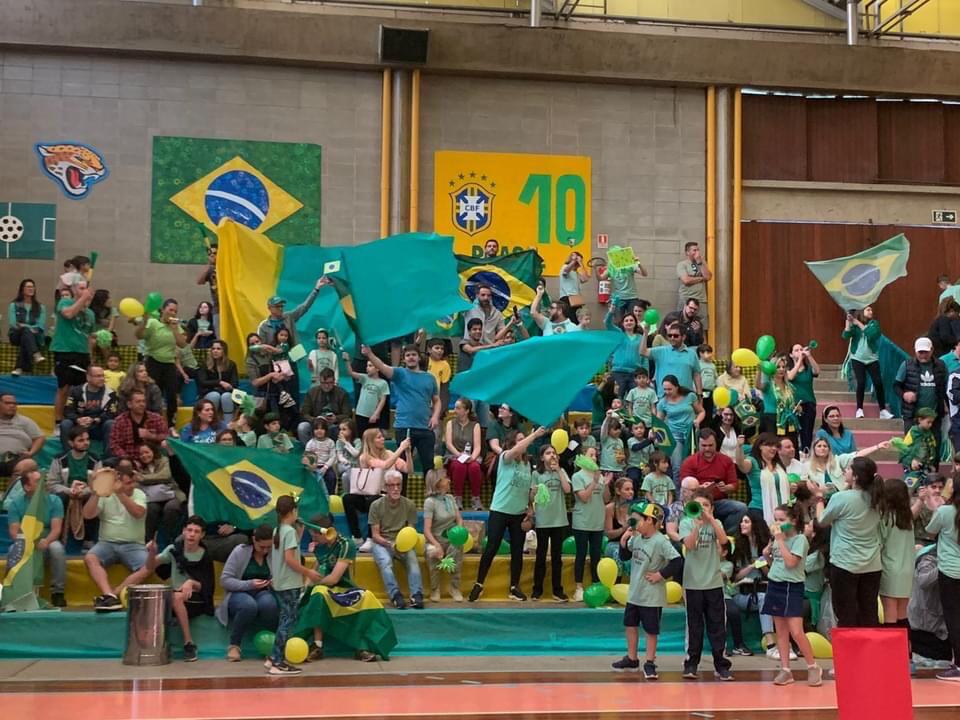 Alunos com bandeiras do Brasil e camisas verdes na abertura da Semana de Esportes