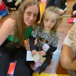 Mãe e filho sentados no chão do ginásio durante a homenagem do Dia das Mães
