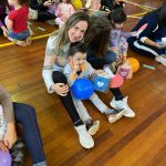 Mãe e filho sentados no chão do ginásio durante a homenagem do Dia das Mães