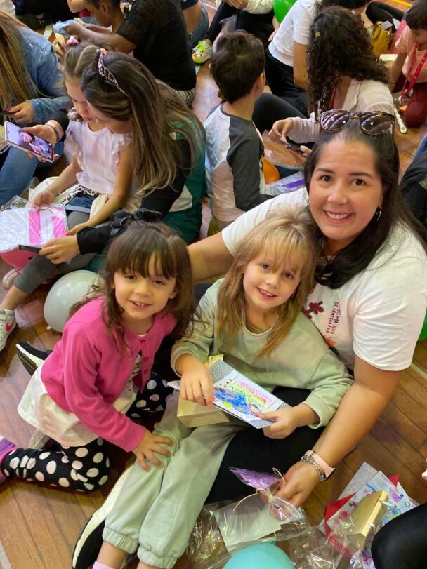 Professora e crianças sentadas no chão com os presentes da homenagem do Dia das Mães