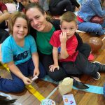 Mãe e filho sentados no chão do ginásio durante a homenagem do Dia das Mães