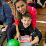 Mãe e filho sentados no chão do ginásio durante a homenagem do Dia das Mães