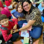 Mãe e filho sentados no chão do ginásio durante a homenagem do Dia das Mães