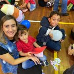 Mãe e filho sentados no chão do ginásio durante a homenagem do Dia das Mães