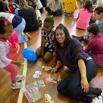 Mãe e filho sentados no chão do ginásio durante a homenagem do Dia das Mães