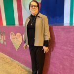 Educadora ao lado do painel decorado com um coração, na homenagem do Dia das Mães
