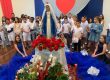 Alunos em volta da imagem de Nossa Senhora enfeitada com flores vermelhas na celebração do mês de Maria