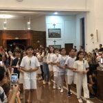 Alunos vestidos de branco em procissão pelo corredor do santuário na coroação de Nossa Senhora