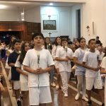 Alunos vestidos de branco em procissão pelo corredor do santuário na coroação de Nossa Senhora