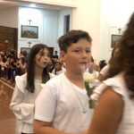 Alunos vestidos de branco em procissão pelo corredor do santuário na coroação de Nossa Senhora