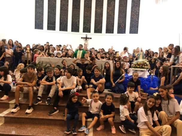 Alunos reunidos em volta da imagem de Nossa Senhora enfeitada com flores na celebração do mês de Maria