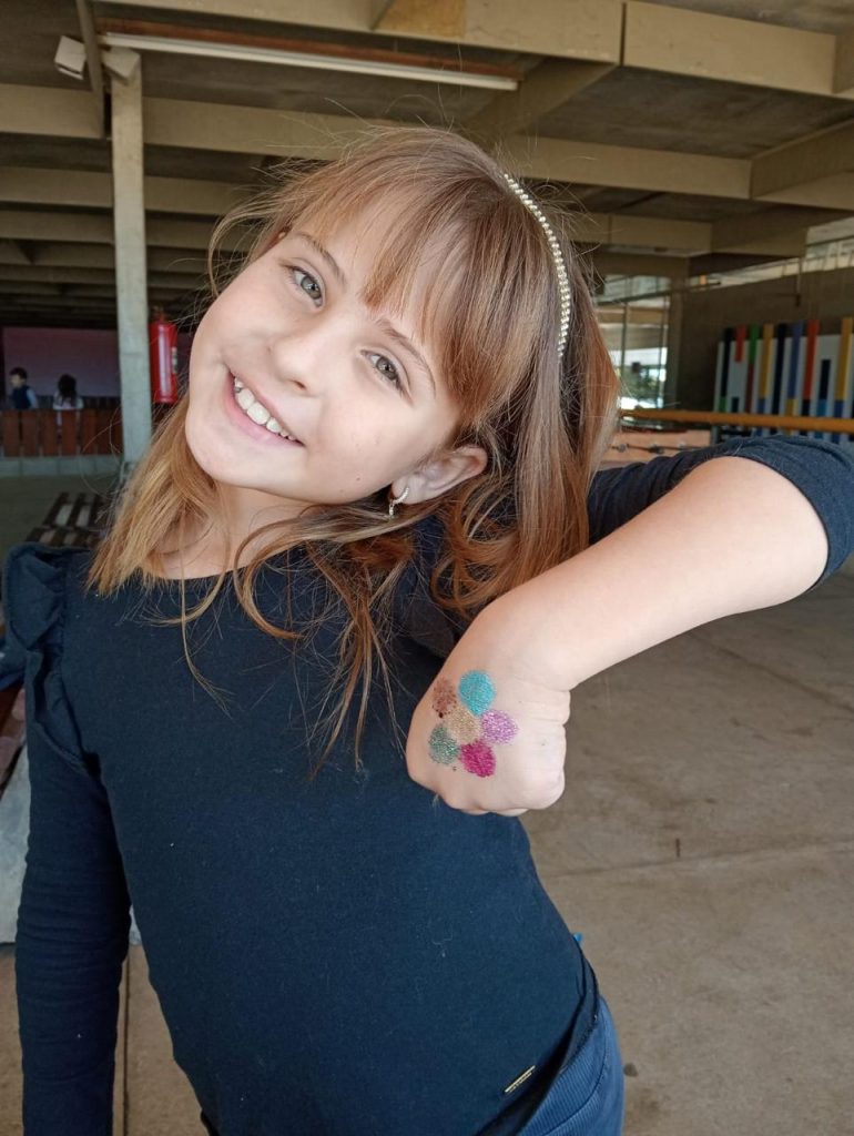 Menina sorrindo e mostrando a pintura colorida no braço durante as férias no Coração