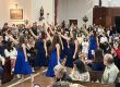 Alunas de vestido azul cantando na capela lotada durante a celebração do mês de Maria