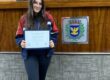 Aluna segurando o certificado do projeto Parlamento Jovem no plenário da Câmara Municipal
