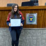 Aluna segurando o certificado do projeto Parlamento Jovem no plenário da Câmara Municipal