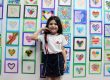 Aluna do Colégio Sagrado diante do painel de desenhos de corações feitos pelos estudantes na Mostra Cultural