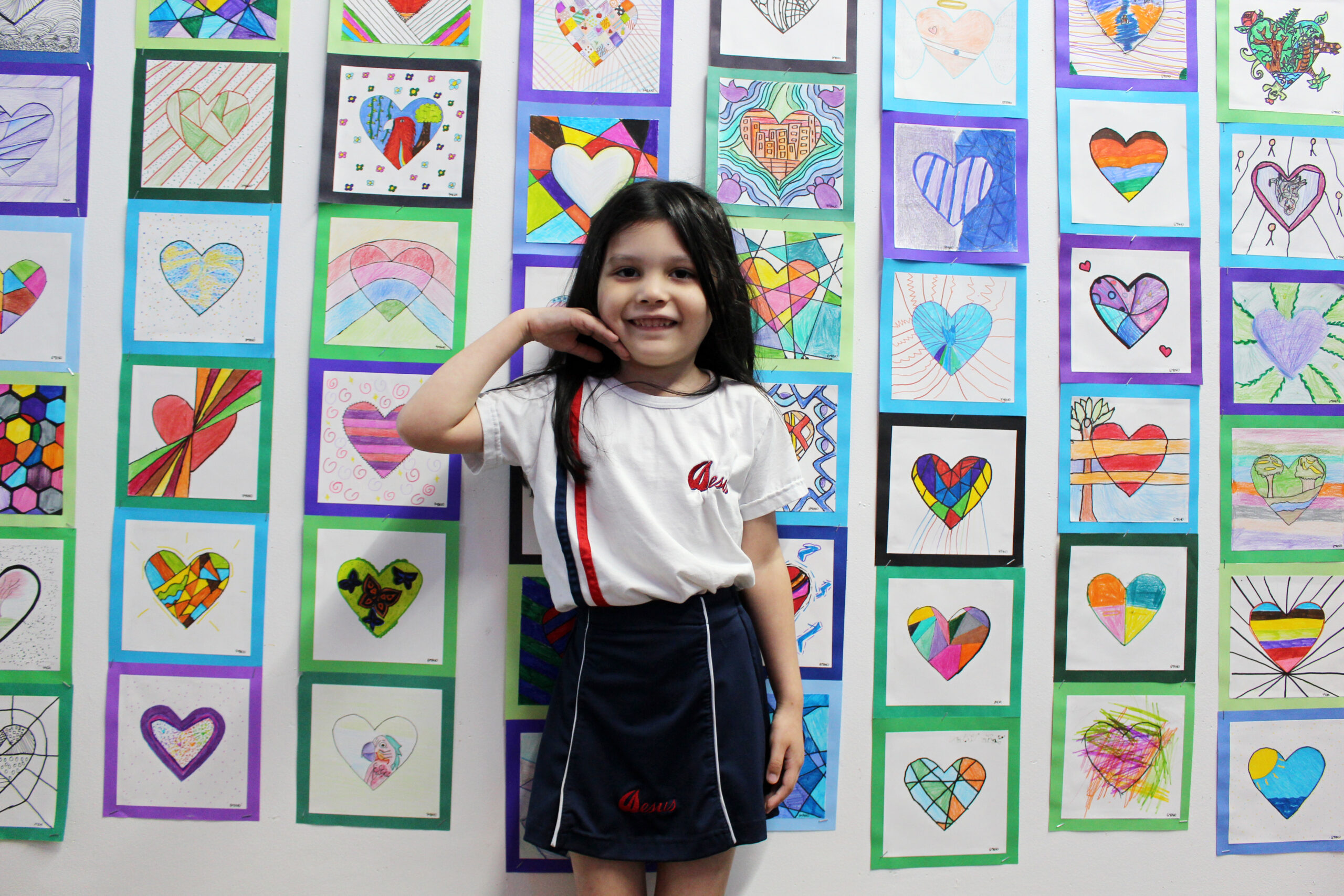 Aluna do Colégio Sagrado diante do painel de desenhos de corações feitos pelos estudantes na Mostra Cultural