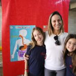 Educadora e alunas posam no estande da Mostra Cultural
