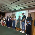 Equipe do colégio perfilada no auditório durante a primeira reunião de pais de 2026, com a projeção ao fundo