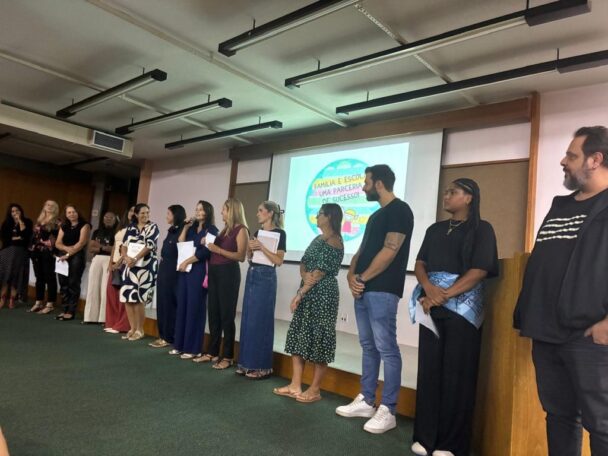 Equipe do colégio perfilada no auditório durante a primeira reunião de pais de 2026, com a projeção ao fundo