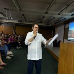 Educadora fala ao microfone no auditório durante a 1ª Reunião de Pais