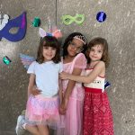 Alunos fantasiados posam diante do painel de máscaras de carnaval do colégio